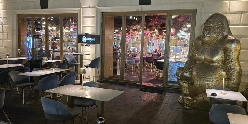 Dehors del cocktail bar a Ostia con tavolini, sedute in velluto e la statua dorata del gorilla